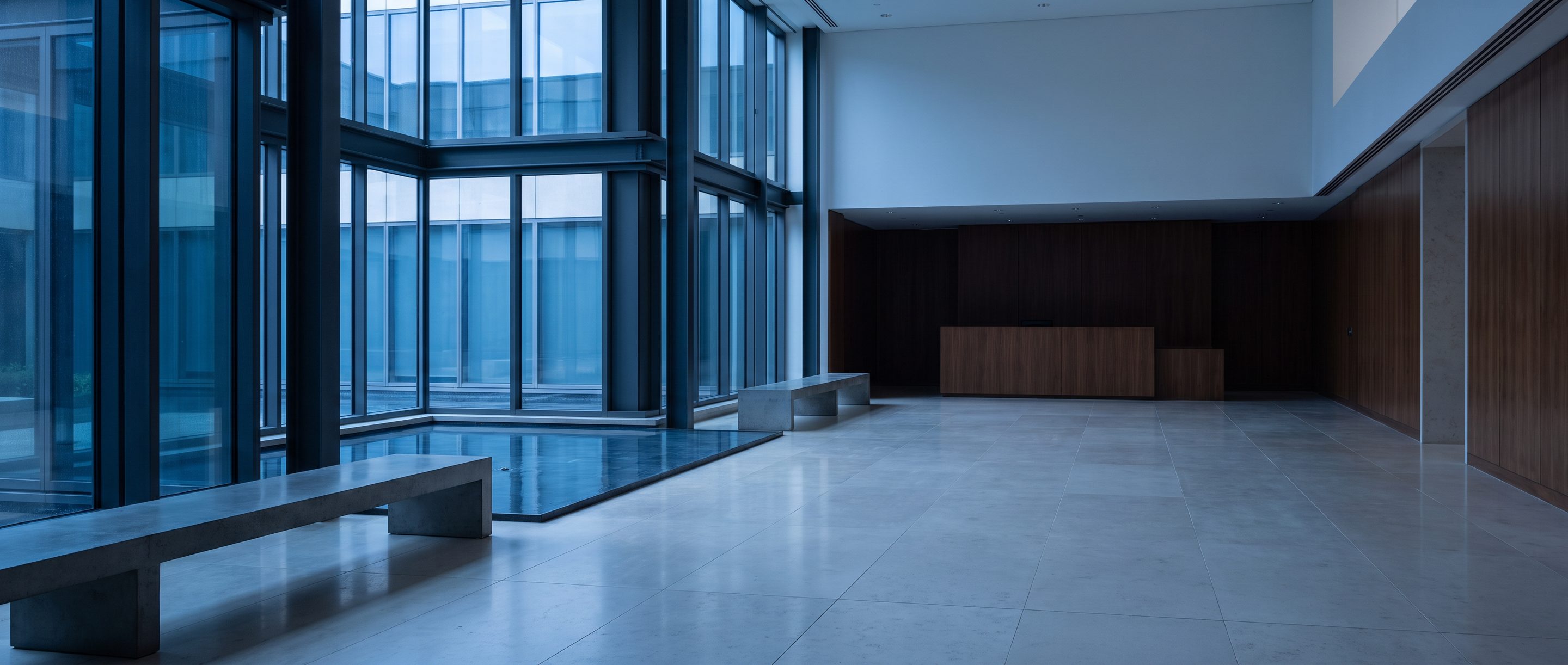A quiet stone-and-glass office lobby, pale limestone floor.