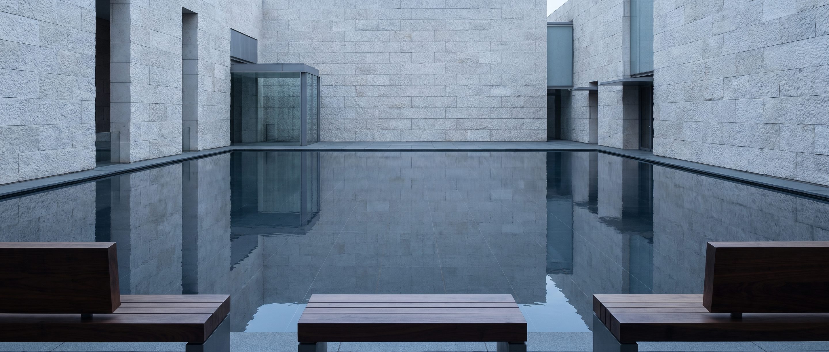 A still reflecting pool against a plain stone wall, overcast light.