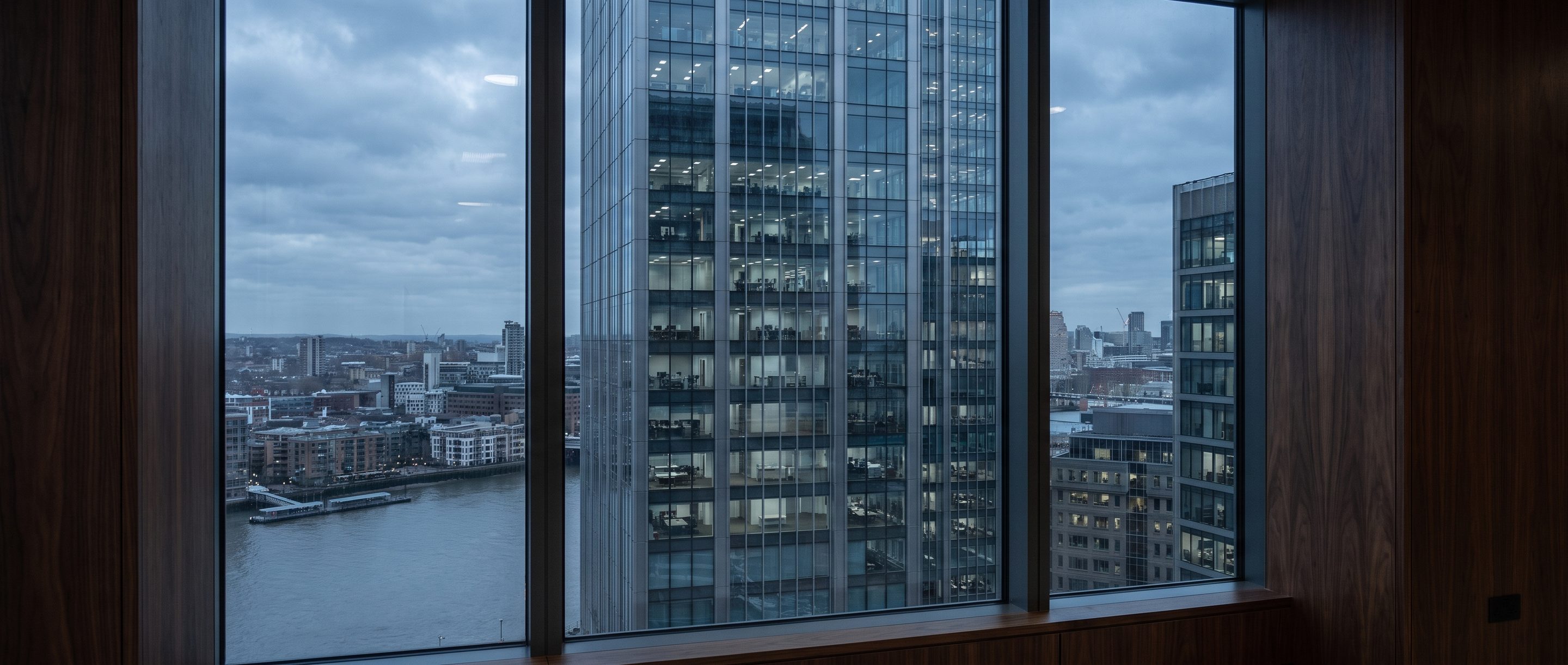 A glass office tower at blue hour seen from a high window.