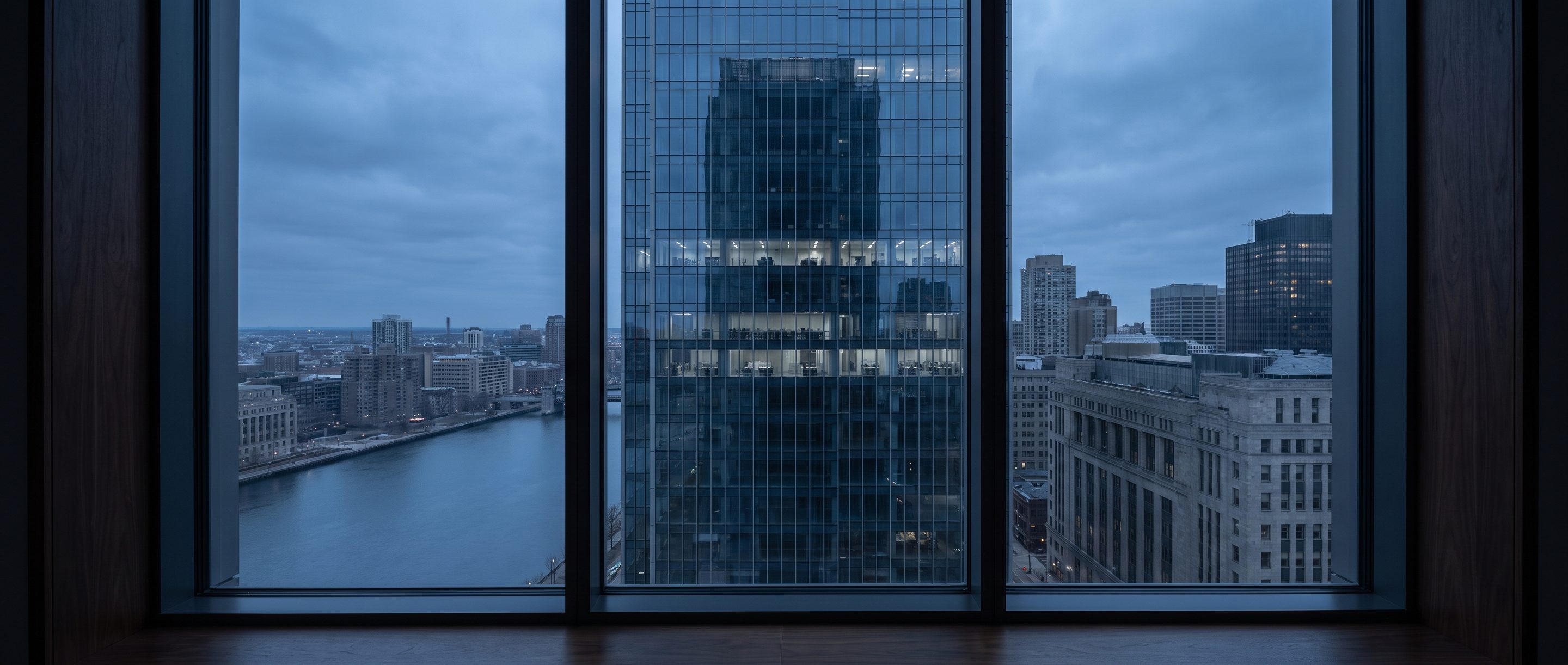 A glass office tower at blue hour seen from a high window.