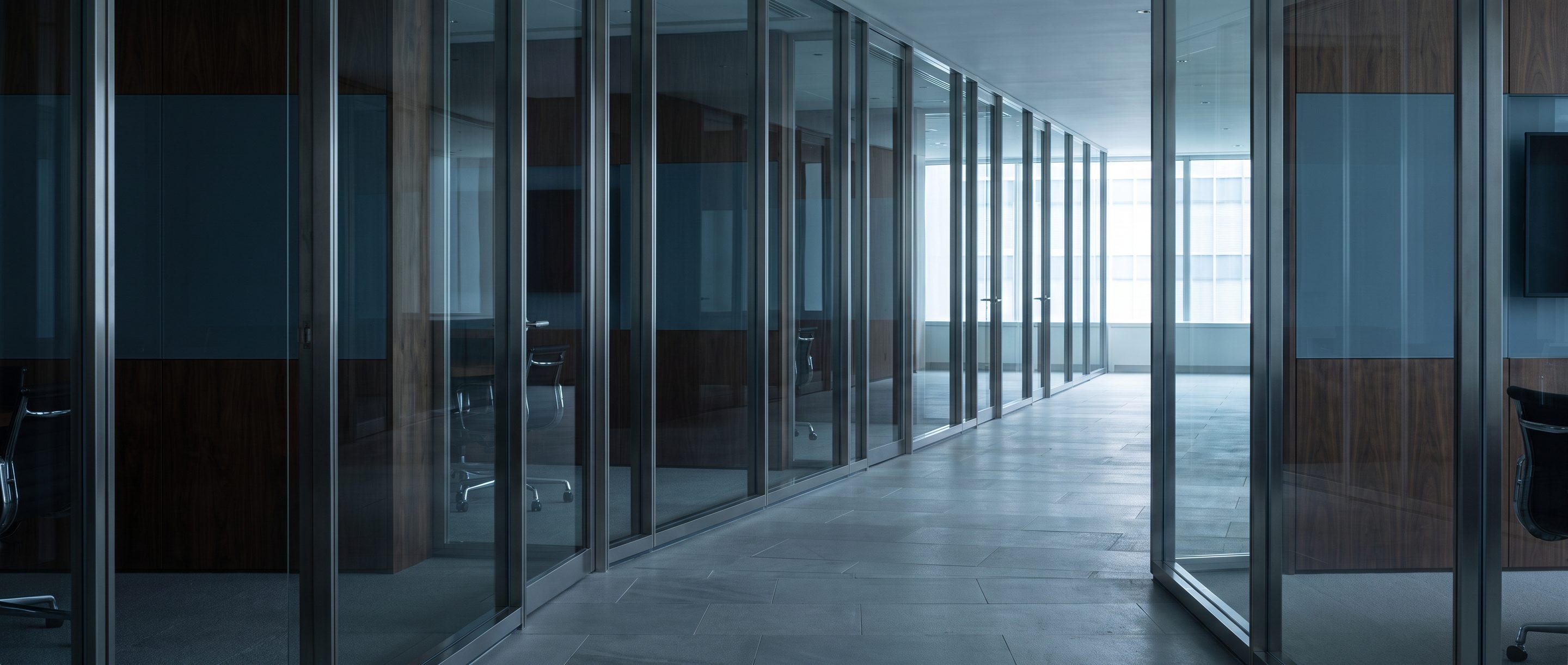 A row of glass-walled meeting rooms along a quiet corridor.