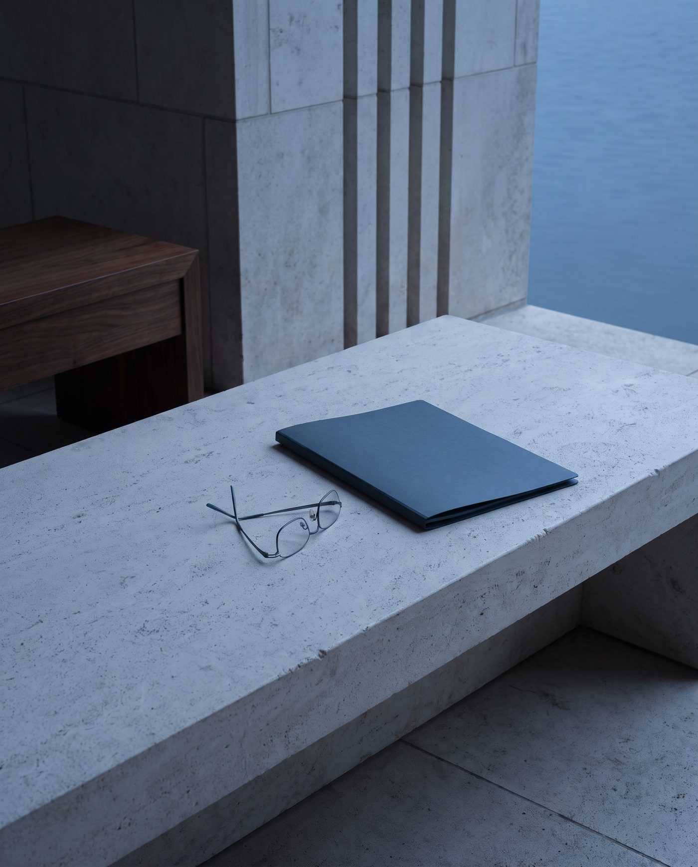 A pair of reading glasses folded beside a closed policy folder on pale stone.