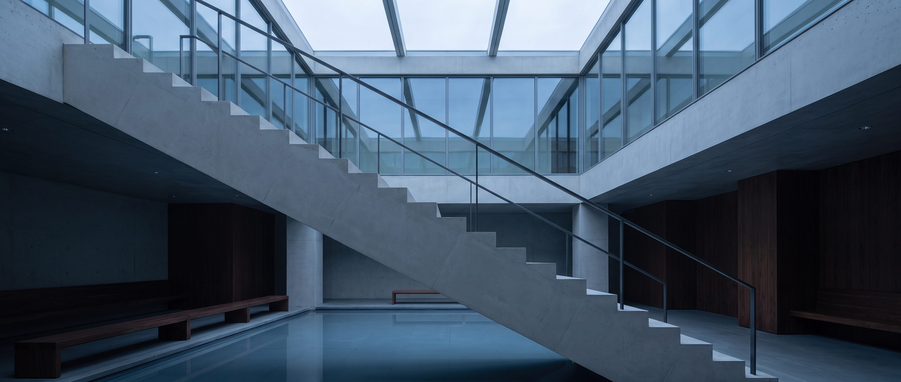 The underside of a pale concrete stair in an empty atrium.