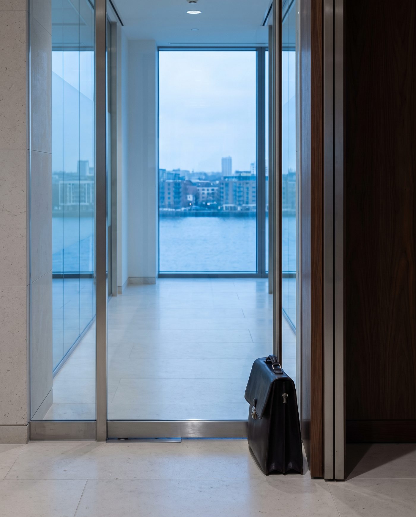 A closed briefcase standing beside a glass office door, corridor light.