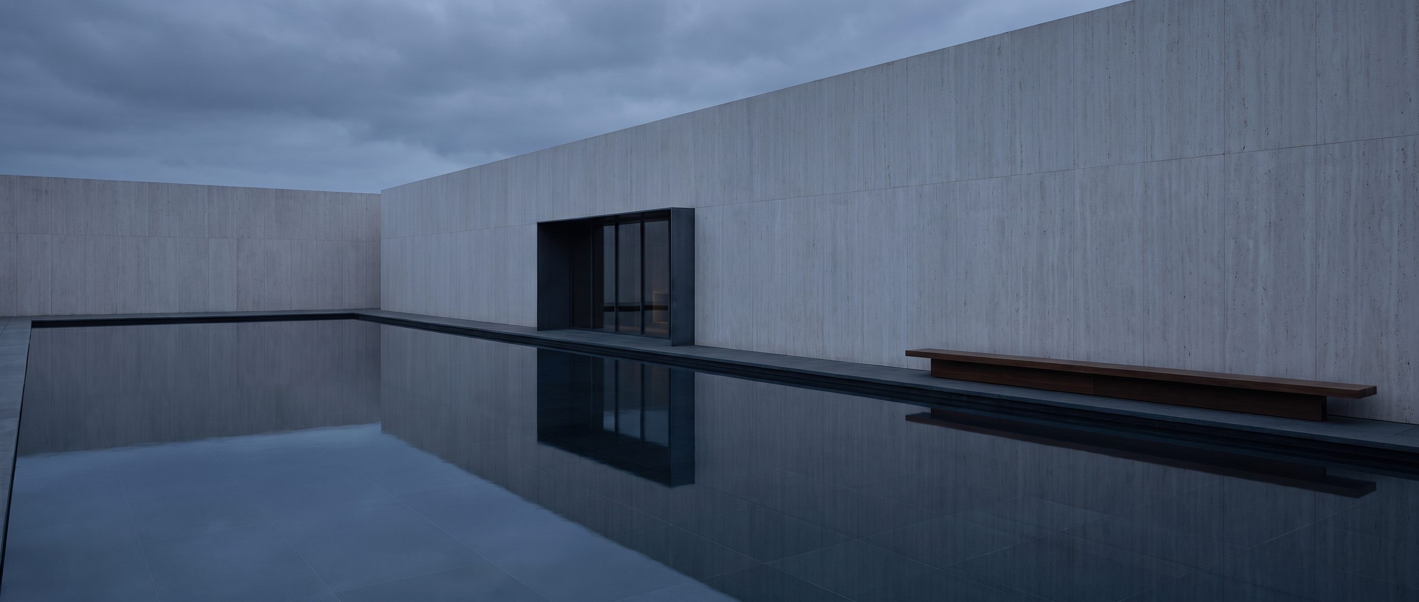 A still reflecting pool against a plain stone wall, overcast light.
