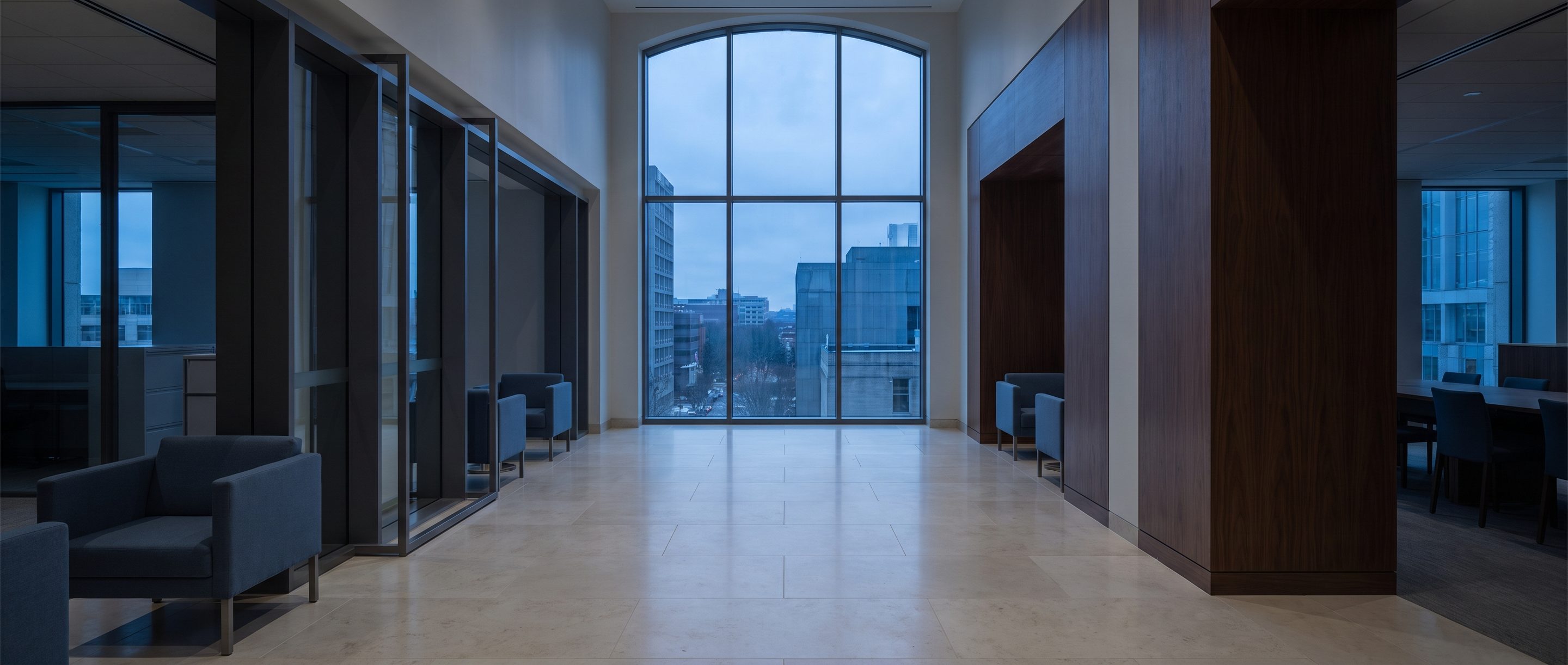 A quiet stone-and-glass office lobby, pale limestone floor.
