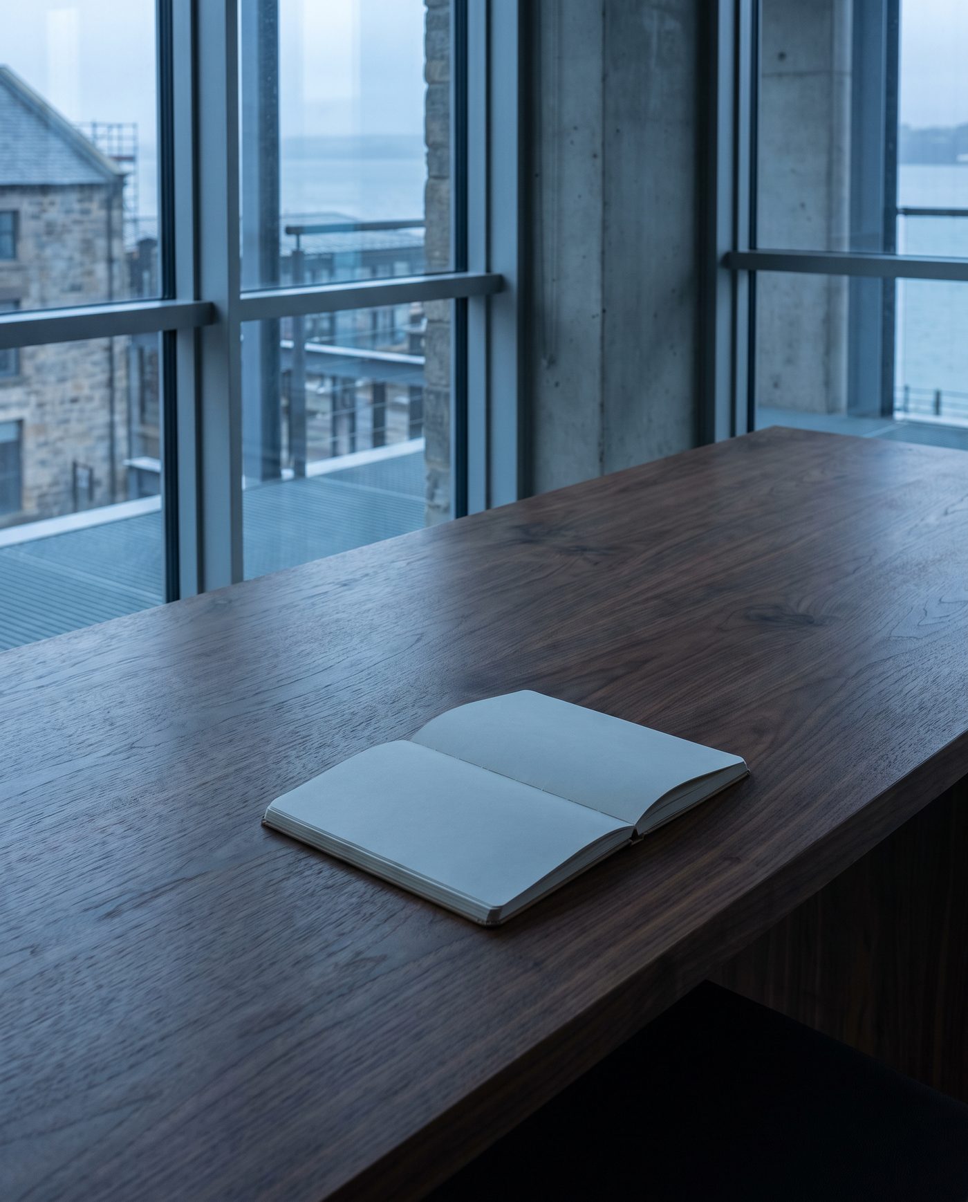 A single blank notebook open on a bare walnut desk, no pen.