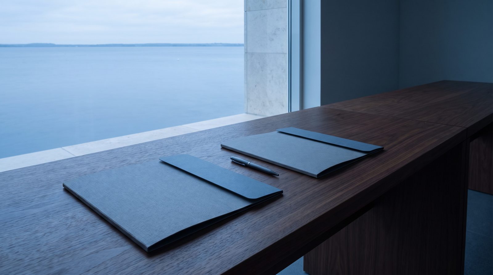 Two folders aligned side by side on a walnut table, a pen between them.