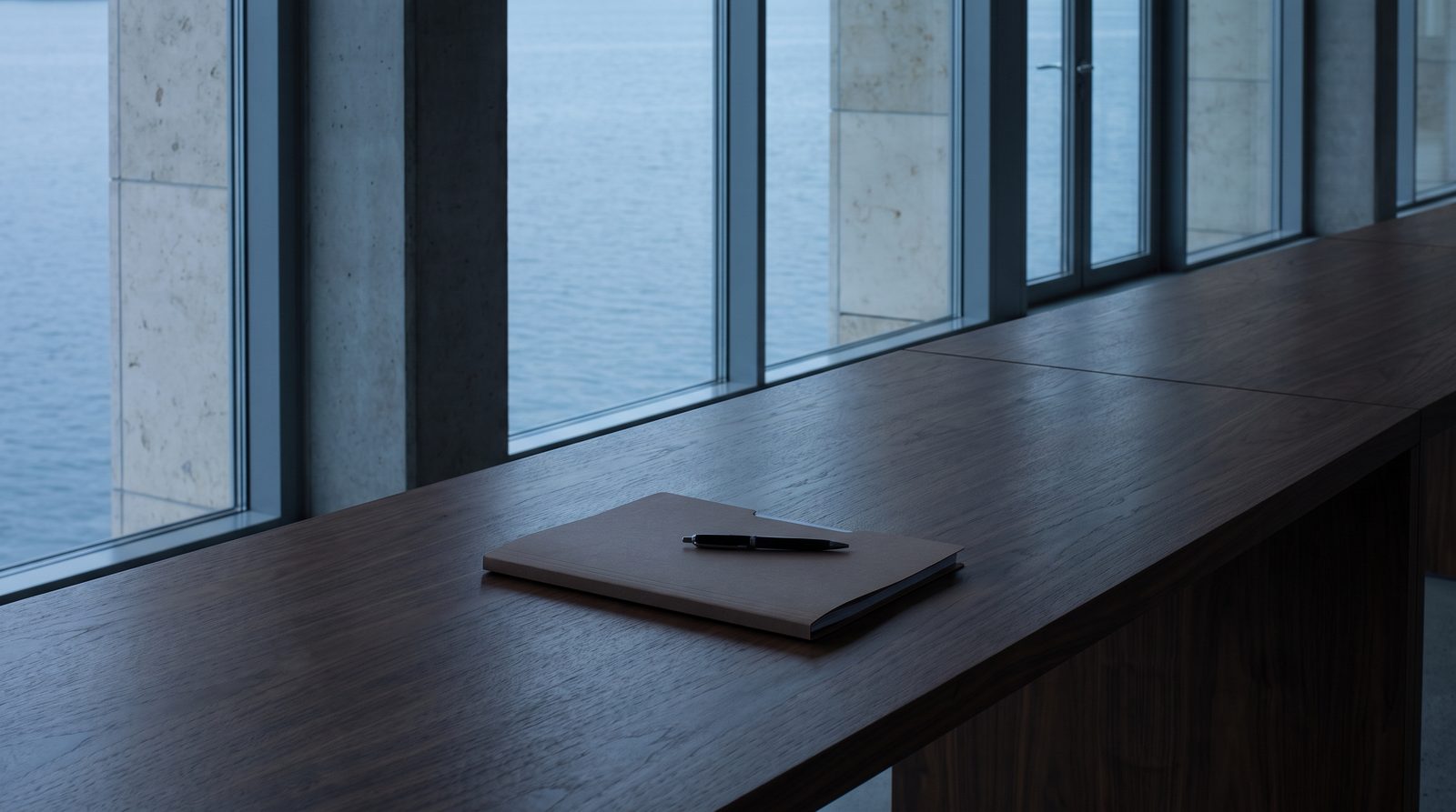 A single signed folder closed on a walnut table, pen resting on top.