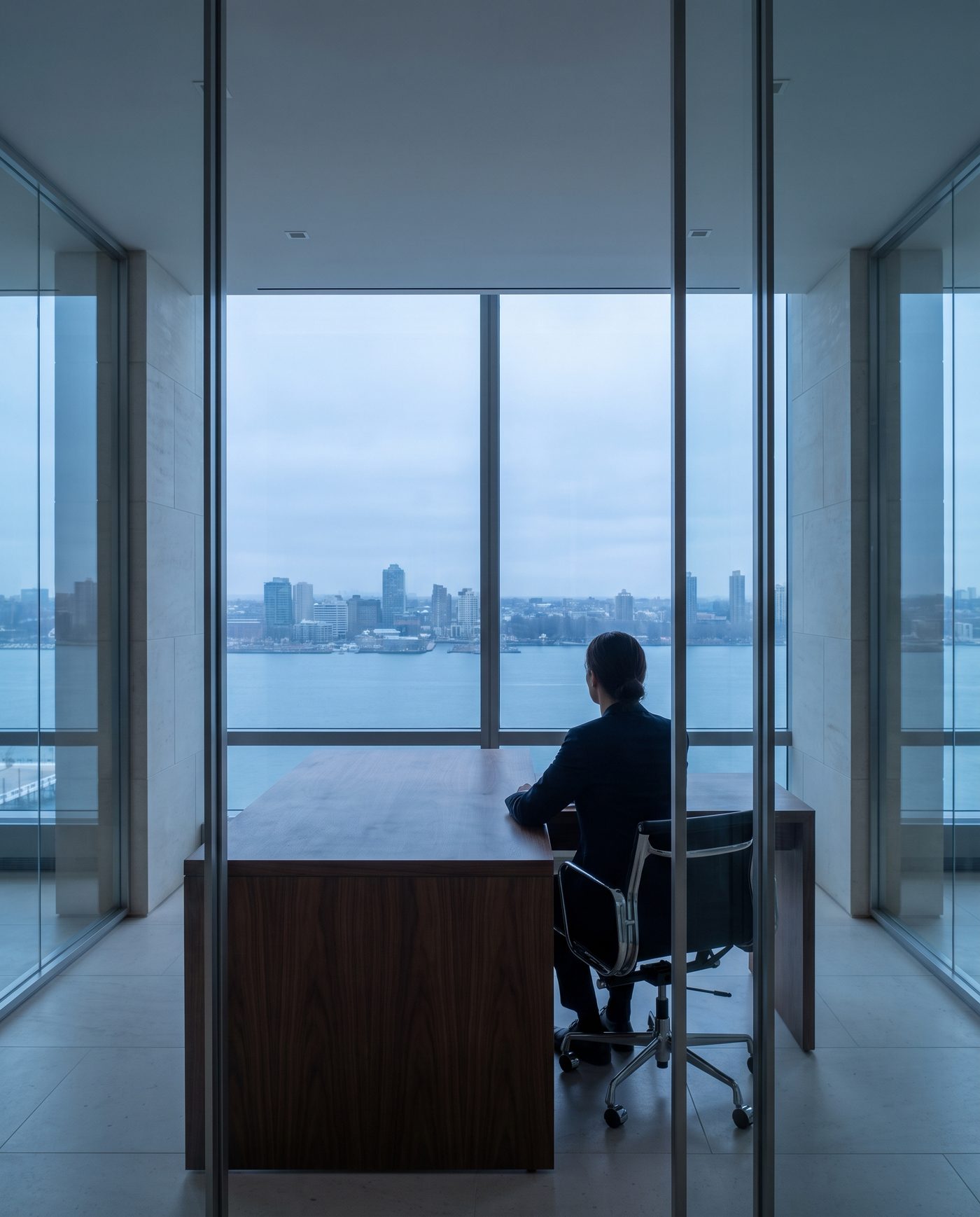 An adult in business dress at a walnut desk, seen from behind.