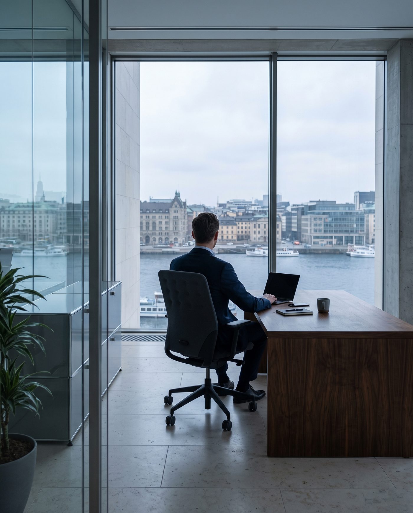 An adult in business dress at a walnut desk, seen from behind.