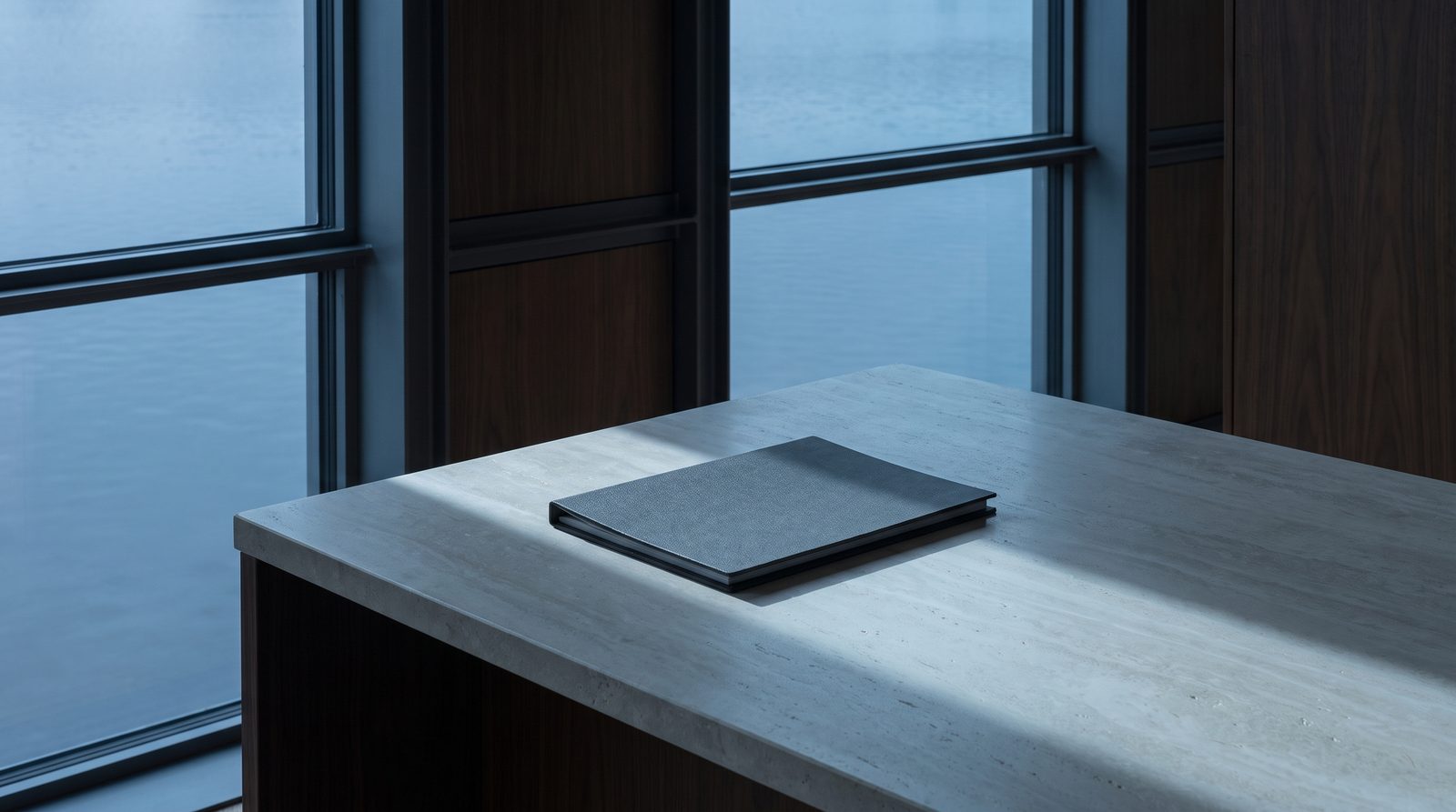 A single closed folder on a pale stone counter, one shaft of window light.