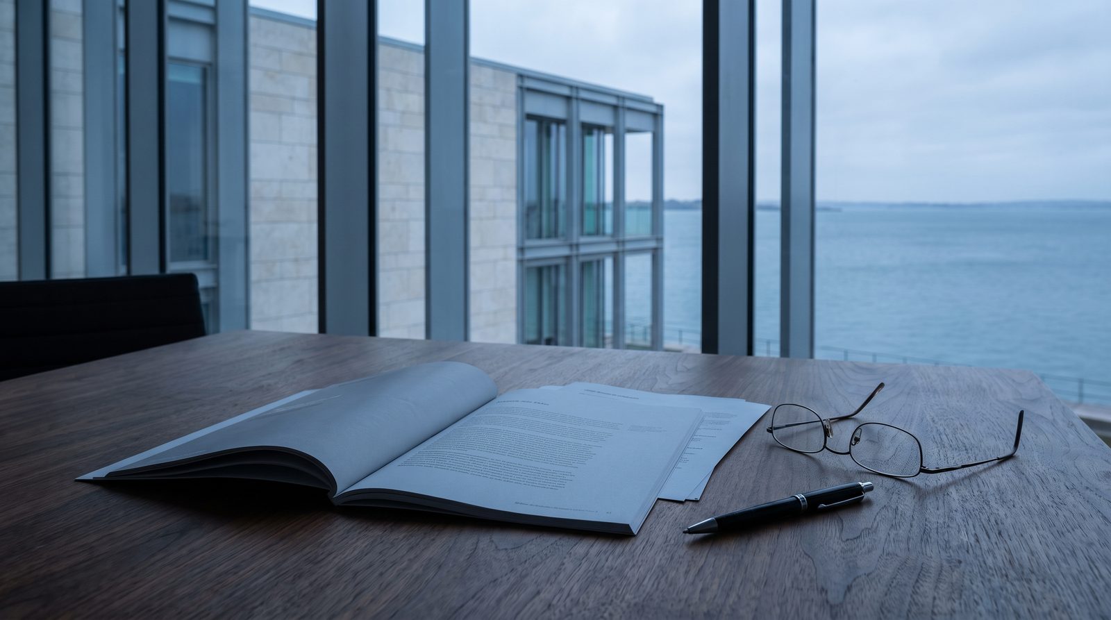 An open report on a walnut table beside reading glasses and a pen.
