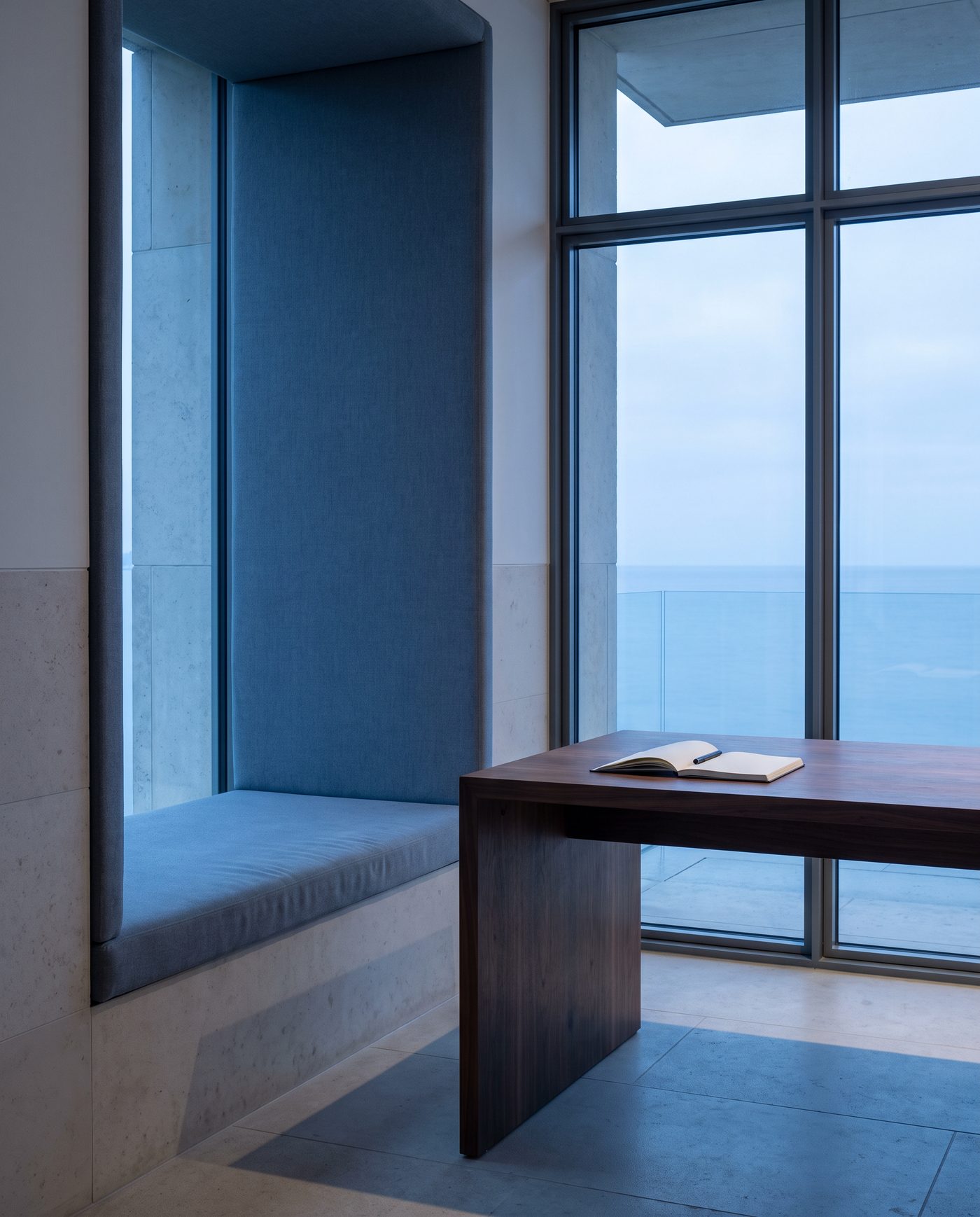 A single tall window seat beside a bare desk, pale morning light.