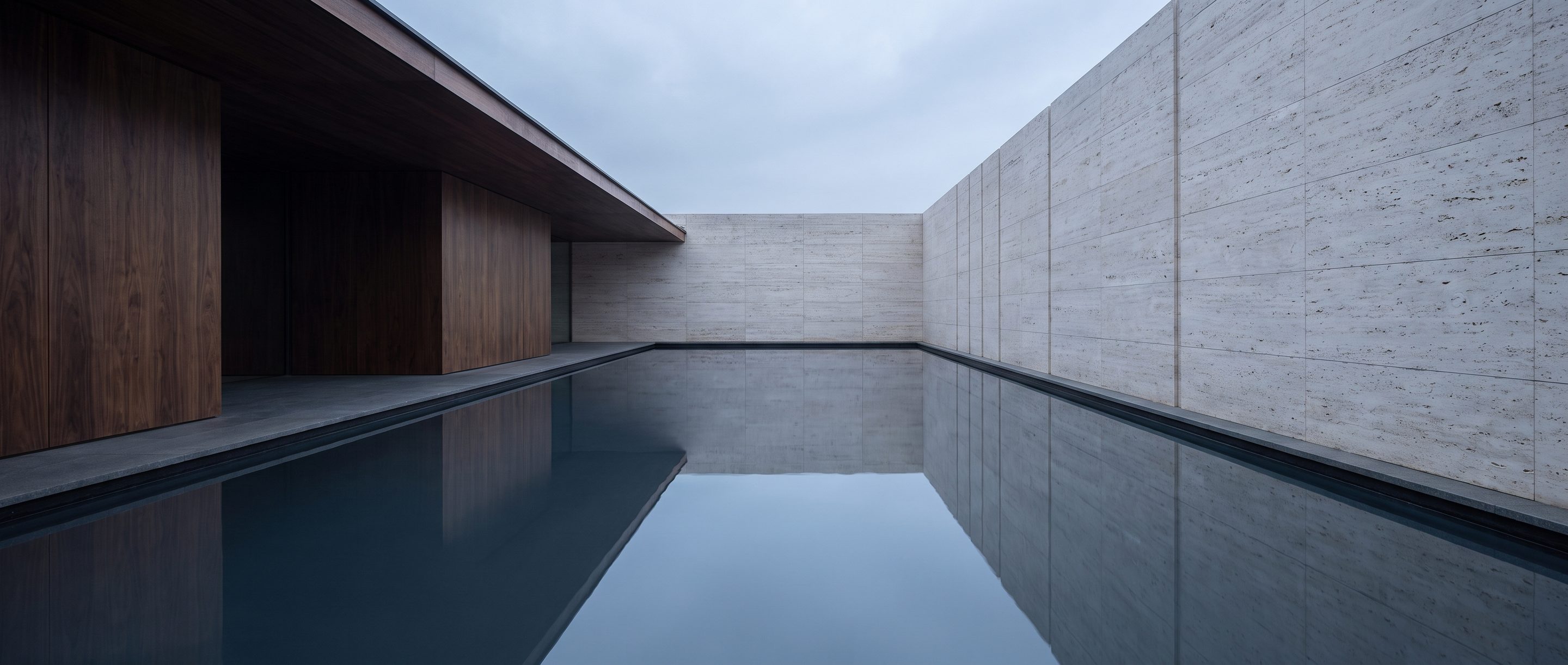 A still reflecting pool against a plain stone wall, overcast light.