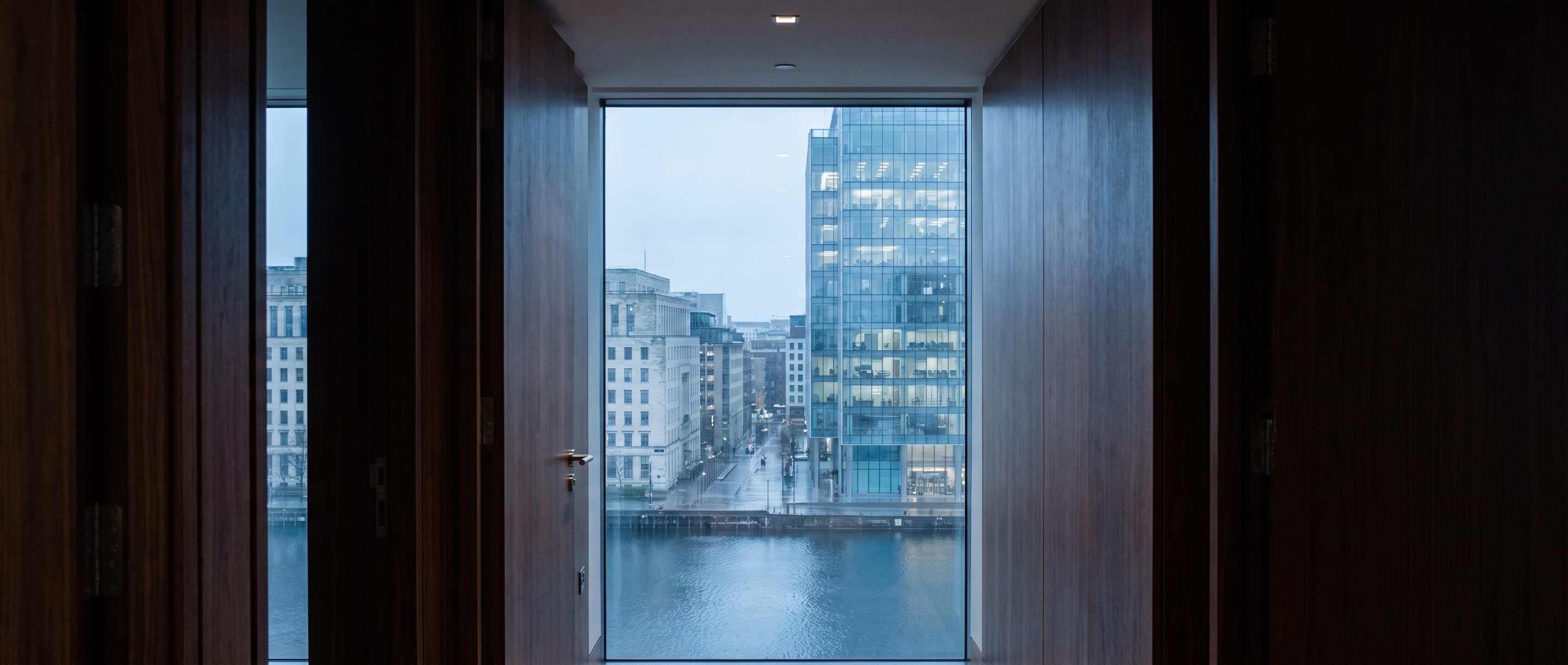A glass office tower at blue hour seen from a high window.