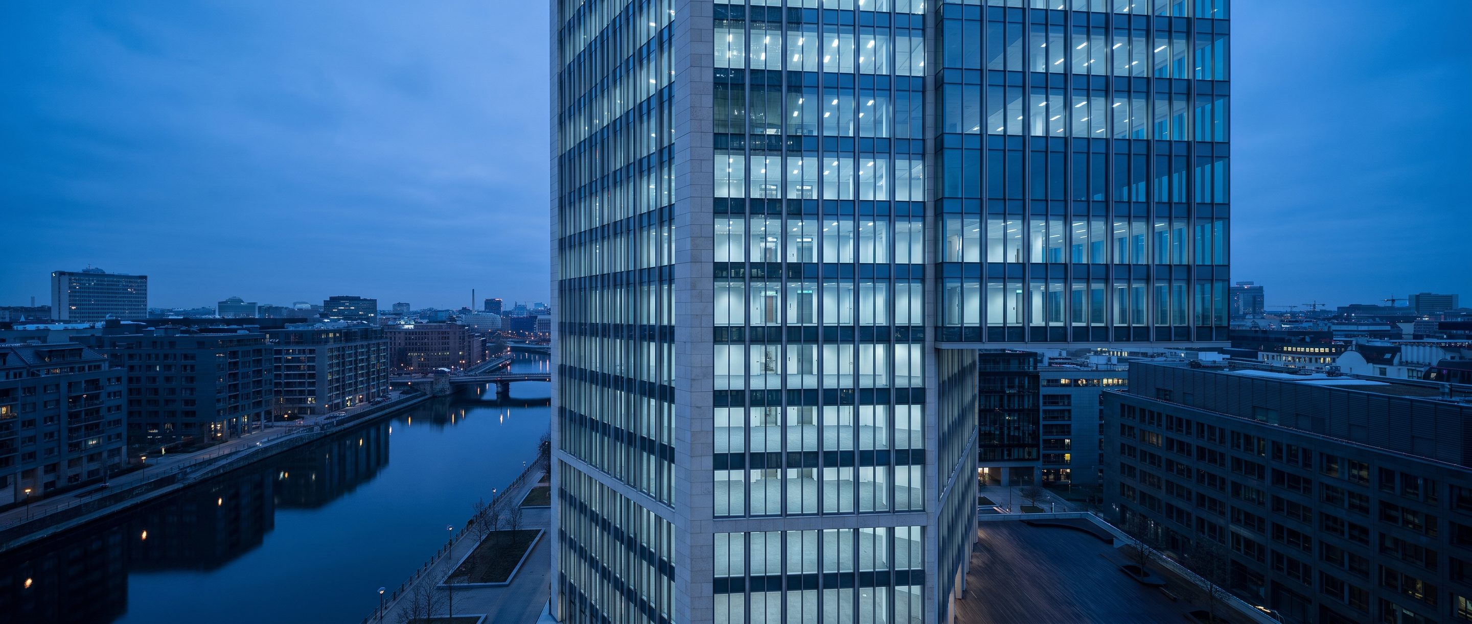 A glass office tower at blue hour seen from a high window.