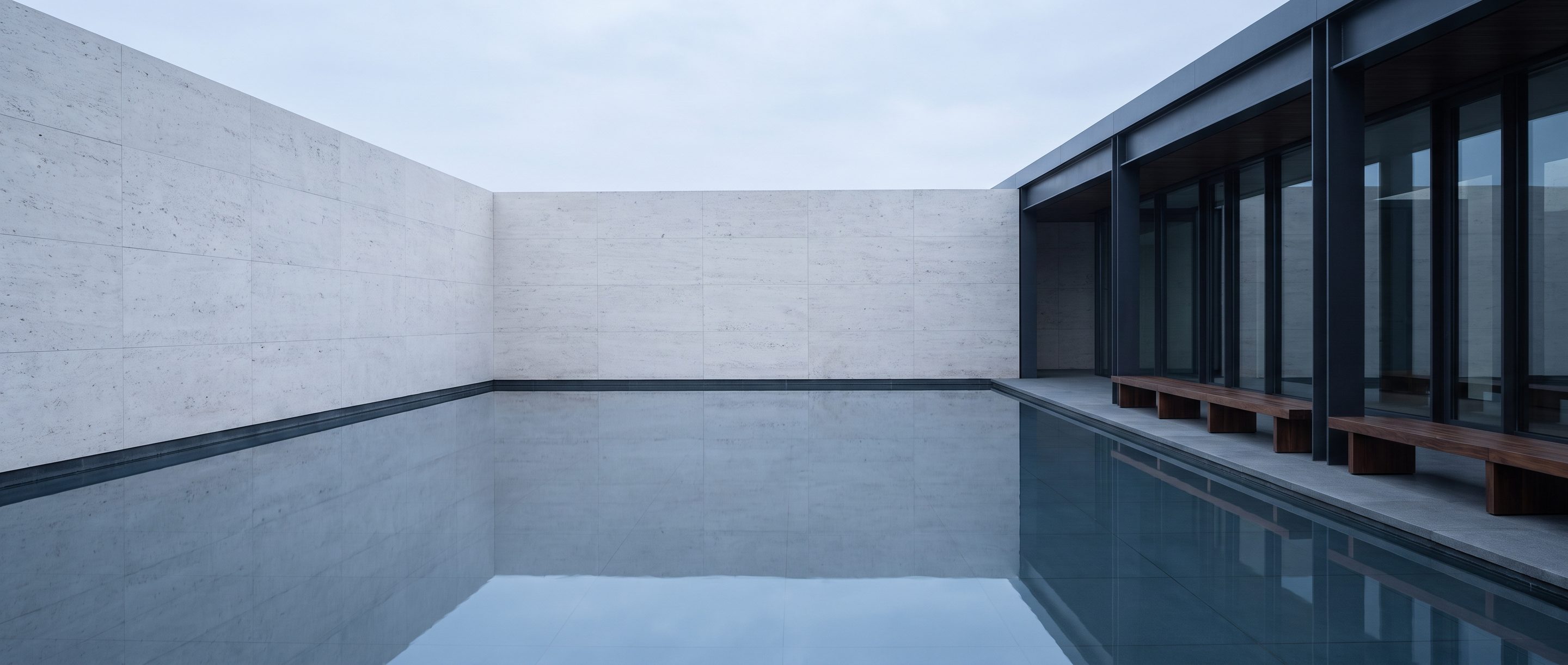 A still reflecting pool against a plain stone wall, overcast light.