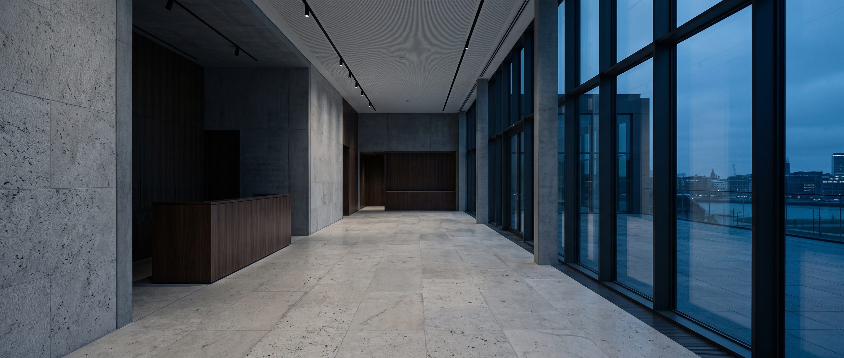 A quiet stone-and-glass office lobby, pale limestone floor.