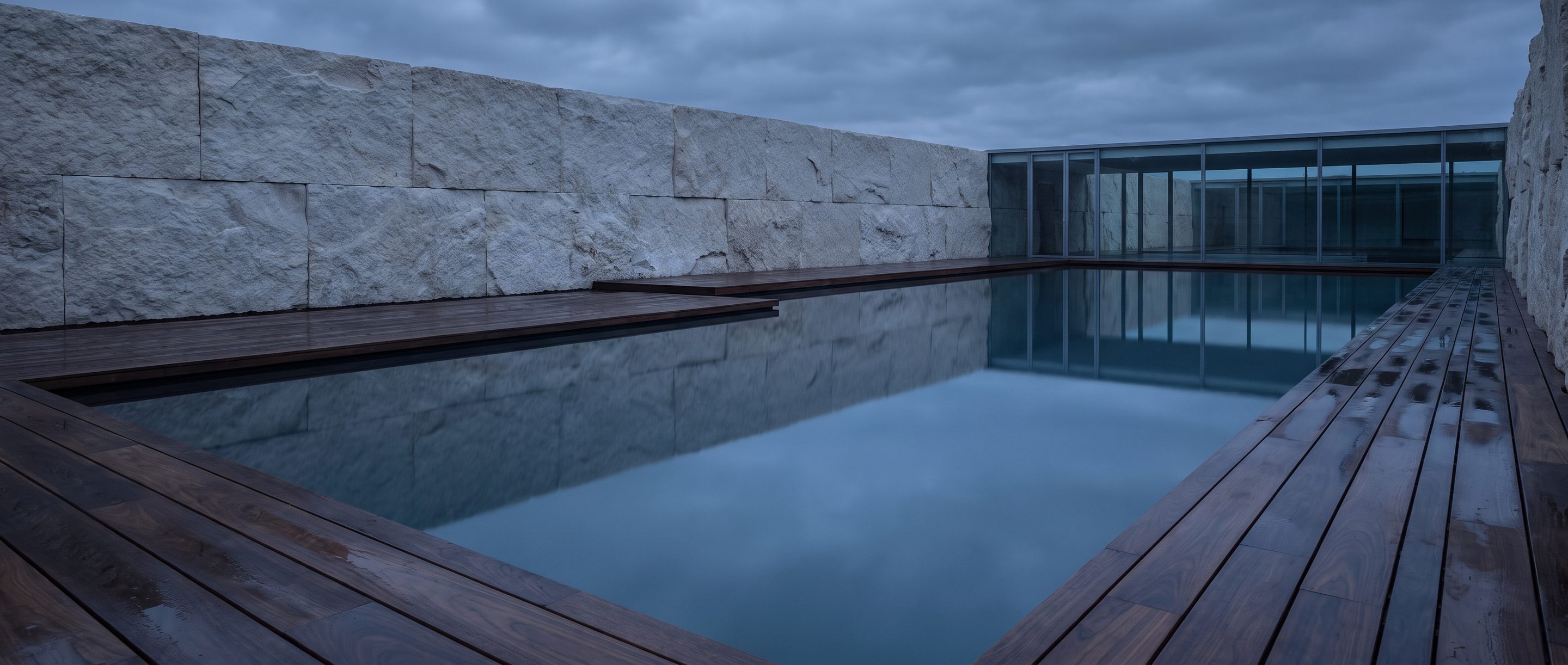 A still reflecting pool against a plain stone wall, overcast light.
